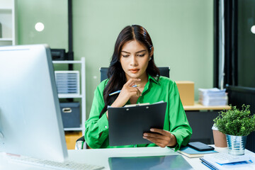 dedicated young Asian businesswoman in a formal suit struggles with stress and office syndrome while working overtime at her desk in a modern glass office. She faces a serious headache and feels sad.