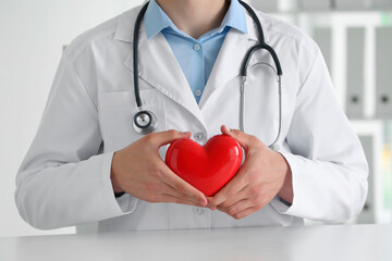 Doctor with red heart at white table in clinic, closeup