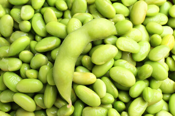 Raw green edamame pod on soybeans as background, closeup
