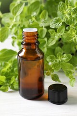 Essential oil in bottle and oregano leaves on white wooden table, closeup