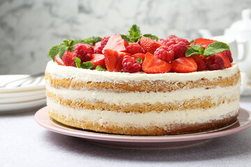 Tasty sponge cake with fresh berries and mint on light gray table