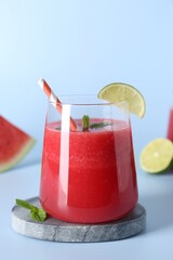 Tasty watermelon drink in glass, mint and fresh fruit on light blue background