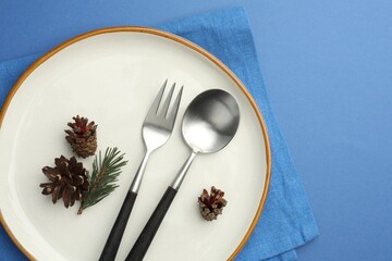 Beautiful Christmas setting with plate, cutlery and cones on blue table, top view