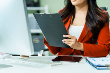 young Asian businesswoman in a formal suit works at her desk in a modern glass office, consulting on LGBTQ-inclusive strategies across various business domains, including HR, IT, and marketing.