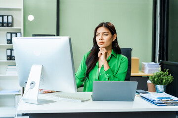 successful and happy young Asian businesswoman in a formal suit works at her desk in a modern glass office. consults on business strategies LGBTQ inclusivity, managing multiple projects efficiently.