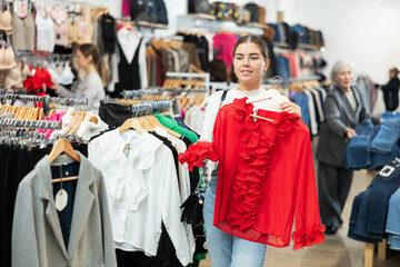 Naklejka premium Smiling young girl choosing colorful clothes in dressing room in showroom