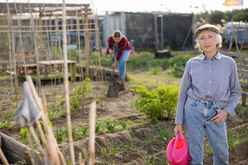 Portrait of an elderly satisfied woman with watering can for watering plants in the garden