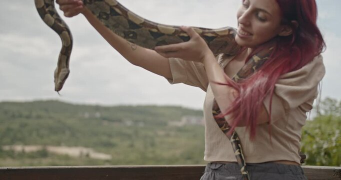 A beautiful young woman with red hair smiles happily as she holds a boa constrictor snake