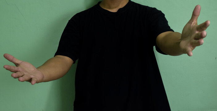 Young man greeting and hugging over on green background. Showing welcome gesture and holding empty raise hands