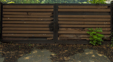An old weathered wooden garage  entrance gate with fallen rotting leaves in the foreground.  