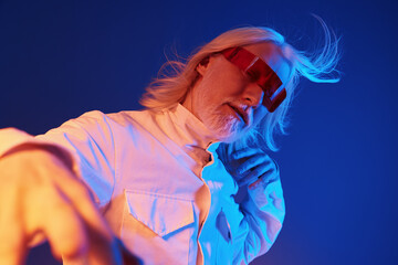 Stylish man with long white hair wearing red sunglasses, posing creatively against a vibrant blue...