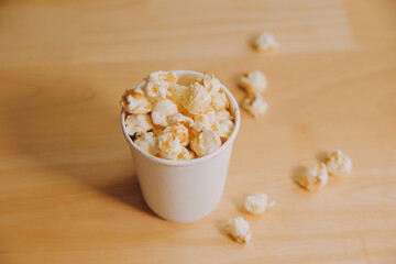 A bucket of popcorn, top-view, warm colors, light brown wooden background, flat lay, daylight macro close-up