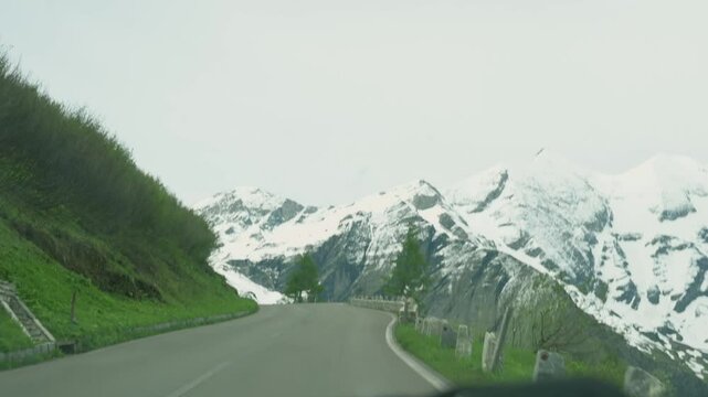 A scenic drive along a winding road through the rocky and snow-dusted terrain of Grossglockner, Austria, with towering cliffs and dramatic alpine views. High quality 4k footage