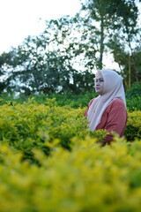a woman wearing a hijab is in the park enjoying flowers and nature