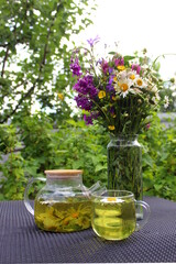 On the table there is a glass teapot and a cup of chamomile infusion.	