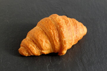 One croissant lies on a black stone tray.