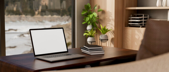 Fototapeta premium A laptop and books on a hardwood table against the window in a contemporary room.