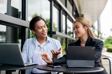 Obraz premium A smart Asian businessman is discussing a project with his assistant at an outdoor table.