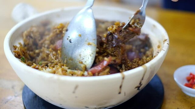 Man mixing bowl of Heung Kee claypot chicken rice with glutinous rice, lap cheong (Chinese sausage), salted fish, spring onion cooked on a traditional charcoal stove - Pudu, Kuala Lumpur, Malaysia