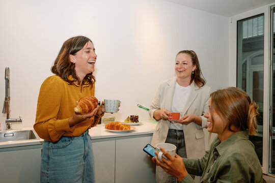Three businesswomen enjoying coffee and pastries during a break in the office kitchen