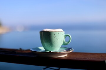 Colorful turquoise coffee cup on table with sea background 