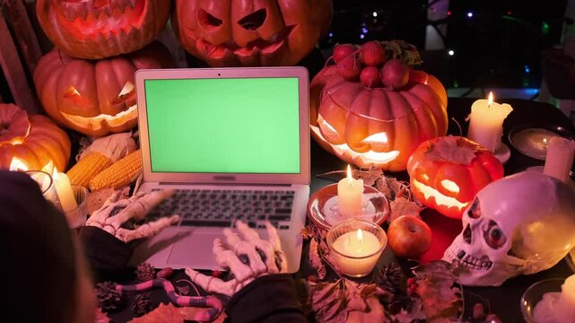 Monster hands typing offers ad promo Halloween at laptop keyboard with green screen with cut out orange pumpkins, candles, skull. Slow motion.