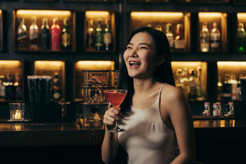 Asian woman drinking a cocktail at a bar at night.