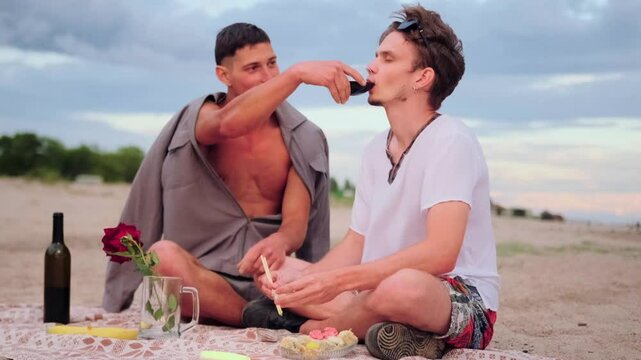 LGBT couple in love enjoying romantic date on beach boyfriend gives his friend red wine while chatting sweetly with each other.