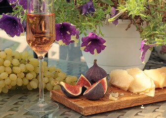 Peeled and cut fresh figs with grapes and cheese, rose wine on terrace sunny day. Food and drink of Mediterranean. Summer and vacation. 