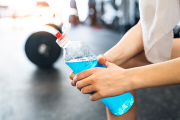 Close up of hands holding blue sport drink after hard workout in gym, side view.