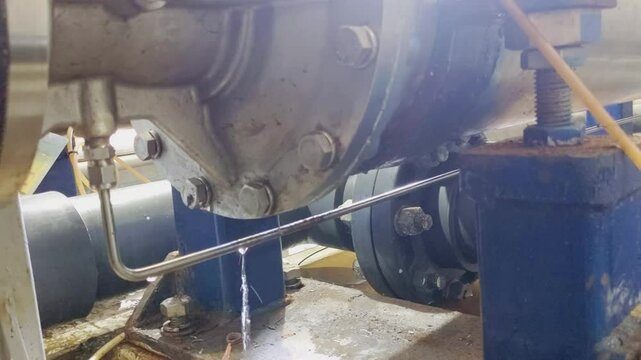Leak in a Mechanical System. A close-up of a leak in a mechanical system, with a steady drip of water coming from a pipe joint