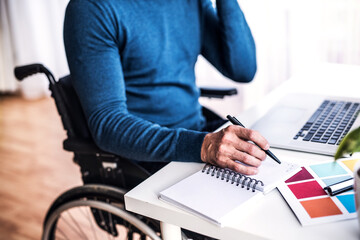 Close up of man in wheelchair working from home office, writing notes in planner. Telecommuting and...