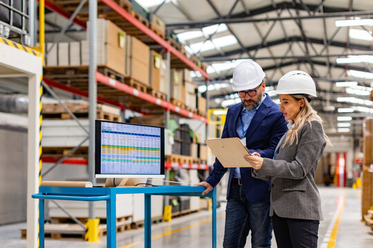 Female engineer and male project manager standing in modern industrial factory by computer, talking about production. Team management in manufacturing facility