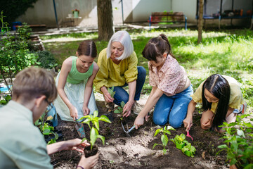 Young kids taking care of plants in school garden during at outdoor sustainable education class,...