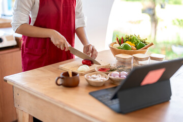 Woman following online cooking course cutting vegetables on wooden board