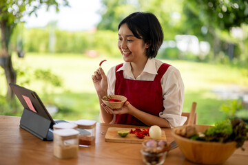 Asian woman following recipe on tablet and holding chili pepper