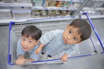 Obraz premium Two young children in shopping cart at store, looking up at the camera with curious and happy expressions.