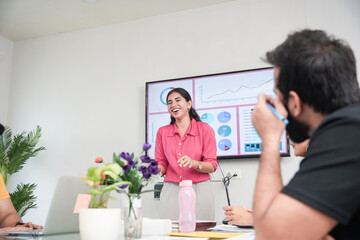 Fototapeta premium Young indian woman at office discussing about business project to team members or colleagues in meeting. Start up, leadership and workplace concept.