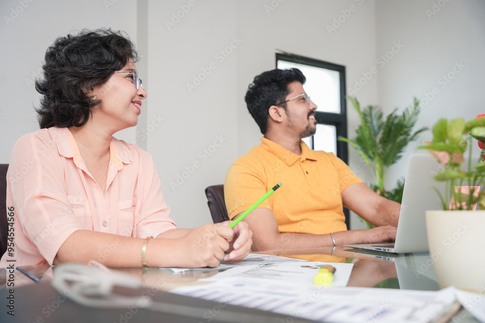 Wall mural two young indian business people sitting around a table during office meeting listening to the prese