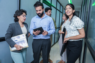 group of young indian corporate business people in formal wear holding reports or documents in hand having a discussion in the office hallway. Teamwork, meeting planning and workspace concept.