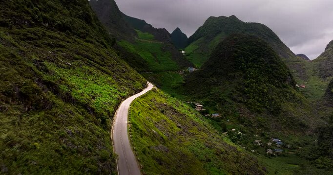 Stunning aerial dolly along winding road cutting through lush green mountains in Ha Giang, Vietnam, offering a serene and picturesque travel route