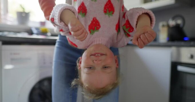 A mother holds her toddler upside down, while playing in the kitchen