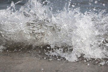 White foam and sea water drop splashes slow motion with sand and blue water