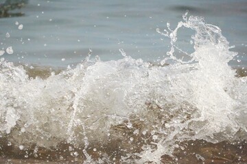 White foam and sea water drop splashes slow motion with sand and blue water