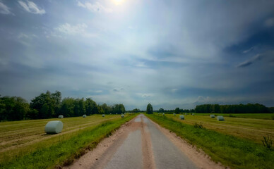 A picturesque and charming rural road adorned with lush fields and hay bales beneath an enchanting sky