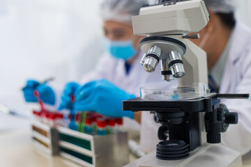 A modern laboratory scene showcasing scientists, both male , in lab coats, analyzing samples using microscopes and computers.
