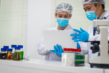 A modern laboratory scene showcasing scientists, both male , in lab coats, analyzing samples using microscopes and computers.