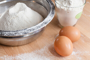 Flour in bowl and two eggs on wooden table background