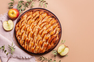 Homemade apple pie with fresh apple fruits on a peach background, top view.