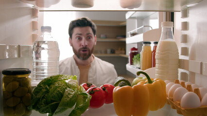 POV point of view from inside refrigerator Caucasian happy funny man adult excited surprised male guy looking in fridge with many food full of organic products say wow kiss tomato delivery supermarket